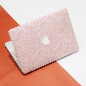 May include: A pink laptop with a decorative floral pattern. The laptop is open, revealing the silver keyboard and screen. The Apple logo is visible on the lid. The background is a split of white and orange.