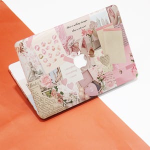 Op de afbeelding: Een roze laptophoes met een collage-ontwerp. Het ontwerp bevat afbeeldingen van bloemen, harten en tekst. De tekst bevat de zinnen "I manifest everything I want" en "there is nothing stronger than a soft soul."