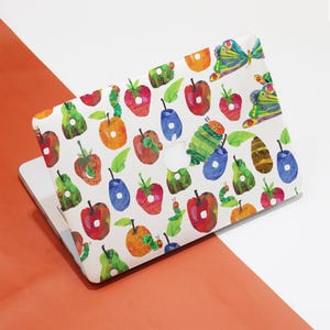 Pode incluir: Uma capa de laptop branca com um padrão colorido de maçãs, peras, ameixas, borboletas e lagartas. O padrão é inspirado no livro infantil "A Lagarta Muito Faminta".