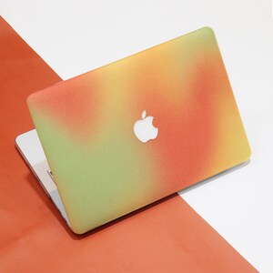 May include: A laptop computer with a colourful ombre design in shades of green, yellow, and orange. The laptop has a white Apple logo on the lid.
