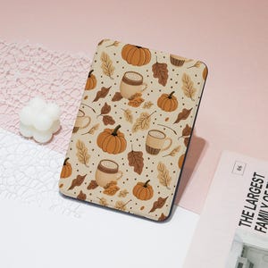 May include: A rectangular case with a beige background featuring a repeating pattern of pumpkins, coffee mugs, and autumn leaves in shades of brown and orange. The case has a black border.