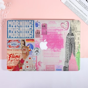May include: Laptop case with a collage design featuring travel-themed graphics. The design includes the text "MORNING!" in large blue letters, along with images of the Empire State Building, travel tickets, and the Statue of Liberty. The Apple logo is visible.