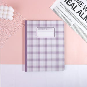 May include: A composition book with a purple and white plaid pattern. The cover features a rectangular label with the words "COMPOSITION BOOK" and a space for a name. The spine is a solid purple color.