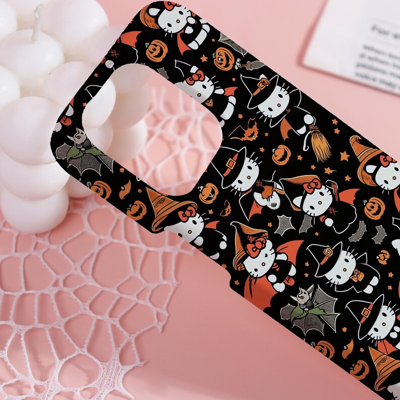 May include: Black phone case featuring a Halloween-themed pattern. The design includes cartoon cats in witch hats and capes, bats, and pumpkins. The case has a glossy finish and a cutout for the camera.