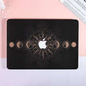 May include: Black laptop case featuring a celestial design with a sunburst, moon phases, and an Apple logo. The design is in gold against a black background. The case has rounded corners and a smooth finish.