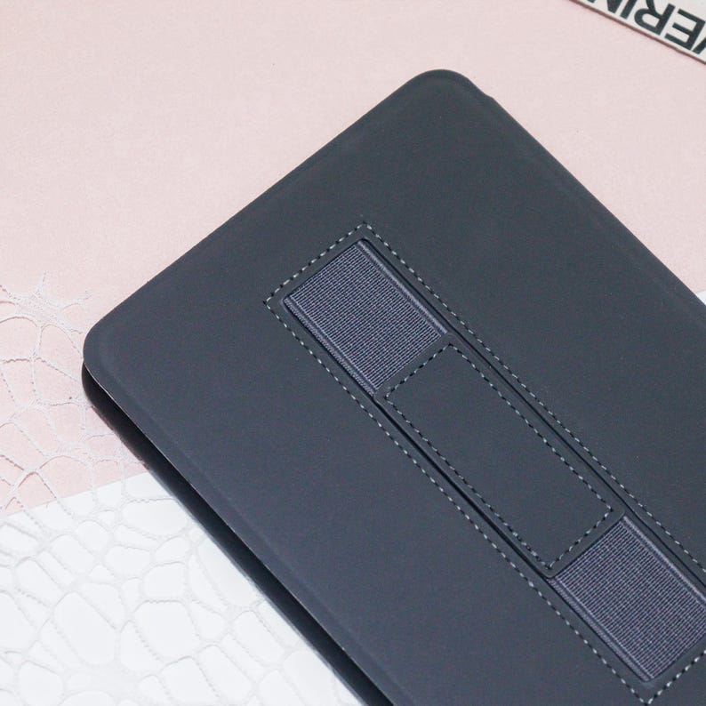 May include: A dark gray tablet case with a textured surface and a built-in elastic band for holding a stylus.