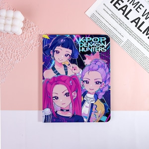 May include: A colorful notebook featuring three anime-style female characters with vibrant hair and stylish outfits. The cover displays the text "KPOP DEMON HUNTERS" in a bold, stylized font, set against a dark background.