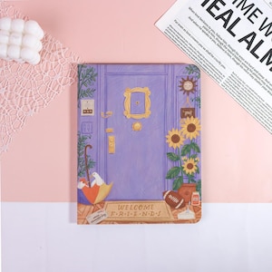 May include: A notebook featuring a purple door design with a gold frame and sunflowers. The notebook has a doormat that says "WELCOME FRIENDS". An umbrella, a football, and a dove are also depicted.