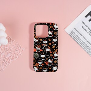 May include: Black phone case featuring a Halloween-themed pattern. The design includes repeating images of a cat character dressed as a witch, along with bats, pumpkins, and stars. The case has a glossy finish and is set against a pink background.