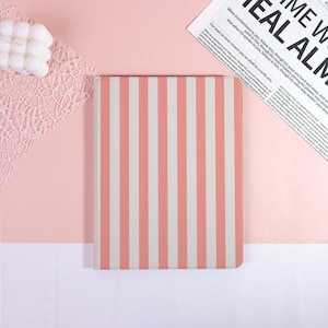 May include: A rectangular notebook featuring a vertical striped pattern in alternating shades of soft coral pink and off-white. The cover has a smooth, matte finish and is positioned centrally, displaying a clean, uniform design across its surface.