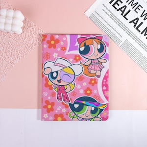 May include: A pink tablet case with a Powerpuff Girls design, featuring Blossom, Bubbles, and Buttercup. The case has a floral pattern and a heart-shaped design. The text "TIME WEAL AL" is visible on a newspaper in the background.