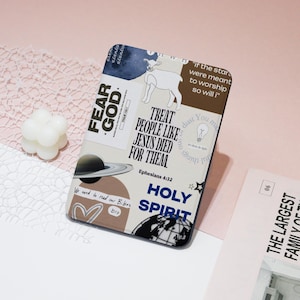 May include: A brown and black Kindle e-reader with a variety of colourful stickers featuring religious and inspirational quotes. The stickers include phrases like "Fear God", "Treat People Like Jesus Died For Them", "Holy Spirit", and "We need to read our Bibles bro".