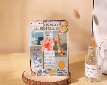 May include: A decorative wooden block featuring a collage of coastal images, including a sailboat, hibiscus flower, and seashells. The block has text that reads "ALOHA HOWDY HELLO" and "WHATS THE BEST THAT COULD HAPPEN". It rests on a wooden slice.