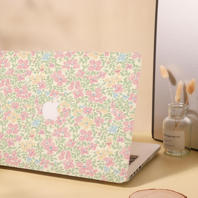 Pu&ograve; includere: Laptop con custodia a fantasia floreale. La custodia presenta un motivo ripetuto di fiori rosa, gialli e blu su sfondo crema. Il logo Apple &egrave; visibile sul coperchio del laptop. Il laptop &egrave; aperto su una superficie chiara.