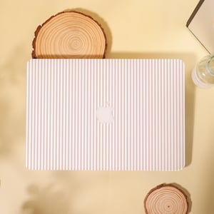May include: A laptop with a pink and white striped pattern. The Apple logo is visible on the back of the laptop. The laptop is on a light yellow surface, with two wooden slices and a glass bottle in the background.