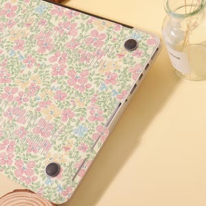 Pu&ograve; includere: Una custodia per laptop con un motivo floreale. La custodia presenta uno sfondo color crema con un motivo ripetuto di fiori rosa, gialli e blu e foglie verdi. La custodia ha una finitura liscia e lucida ed &egrave; progettata per proteggere il laptop.