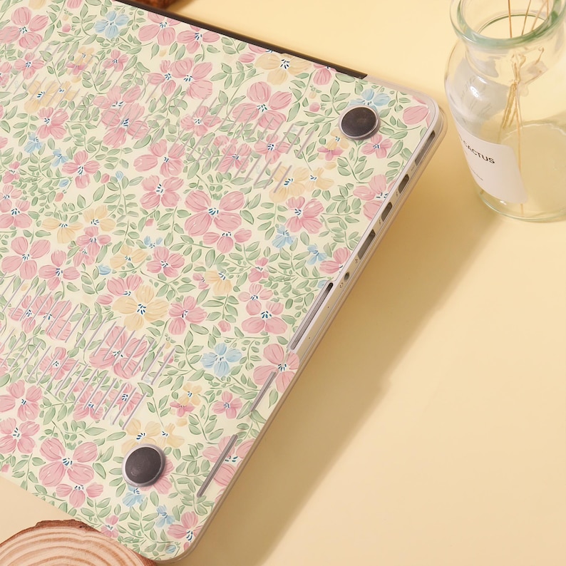 Pu&ograve; includere: Una custodia per laptop con un motivo floreale. La custodia presenta uno sfondo color crema con un motivo ripetuto di fiori rosa, gialli e blu e foglie verdi. La custodia ha una finitura liscia e lucida ed &egrave; progettata per proteggere il laptop.
