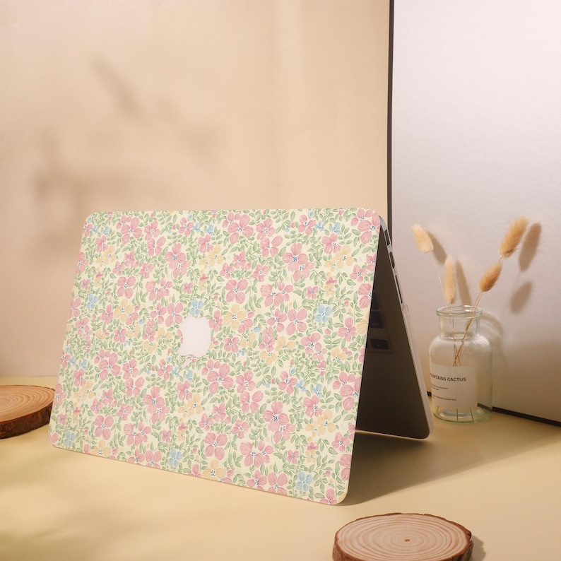 Pu&ograve; includere: Un laptop con una custodia a fantasia floreale. La custodia presenta un motivo di fiori rosa, gialli e blu su uno sfondo giallo chiaro. Il logo Apple &egrave; visibile.