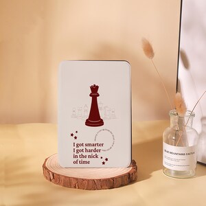Peut inclure: Plaque rectangulaire blanc cassé avec une illustration d'une reine d'échecs marron et du texte. Le texte dit : « I got smarter, I got harder in the nick of time ». La plaque est présentée sur une tranche de bois.