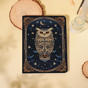 May include: A dark blue journal featuring an owl illustration. The owl is detailed with brown and beige feathers, set against a starry night sky with a crescent moon and stars. The journal has a decorative border.
