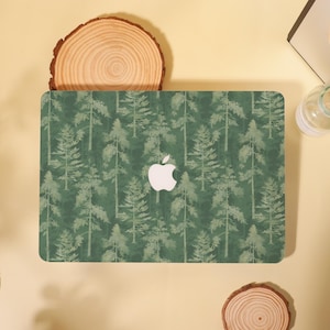 Könnte beinhalten: Eine grüne Laptop-Hülle mit einem Waldmuster und weißen Baum-Silhouetten. Die Hülle hat ein weißes Apple-Logo. Das Design ist ein sich wiederholendes Muster von Bäumen auf grünem Hintergrund.