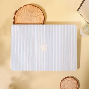 May include: A laptop with a light blue and white striped design. The Apple logo is visible in the center. The laptop is on a light yellow surface, with two wooden slices and a glass bottle in the background.