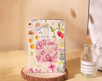 May include: A white notebook cover with a colorful illustration of a strawberry plant, a croissant, a laptop, a pair of boots, and other whimsical details. The text "I hope you know everything is going to be okay" is written in pink on the cover.