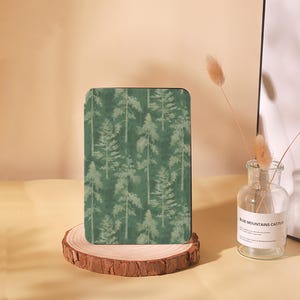 May include: A green e-reader cover with a forest pattern. The cover is on a wooden stand.