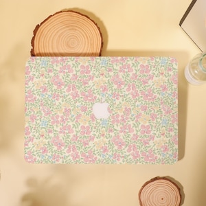 May include: A laptop case with a floral design. The case has a pale yellow base, adorned with pink, blue, and yellow flowers and green foliage. The Apple logo is centrally placed.