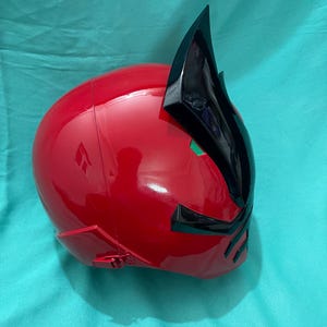 May include: A red and black plastic helmet with a pointed crest. The helmet has a glossy finish and is designed to resemble a character from a popular television show.