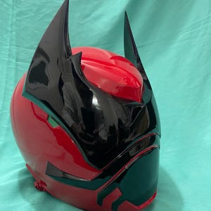 May include: A red and black helmet with a pointed design. The helmet has a black visor and two black horns on top.