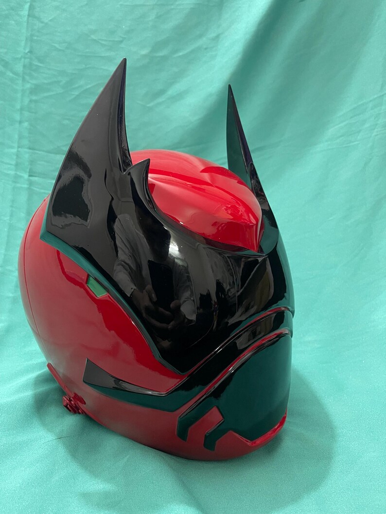 May include: A red and black helmet with a pointed design. The helmet has a black visor and two black horns on top.