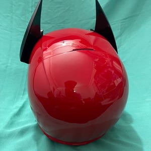 May include: A red motorcycle helmet with black horns attached to the top.