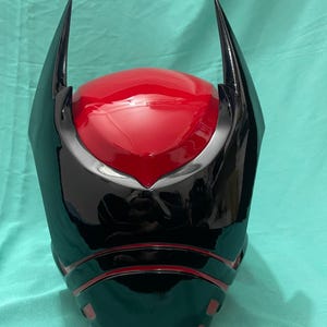 May include: A black and red helmet with a pointed design on the top. The helmet has a glossy finish and a red visor.