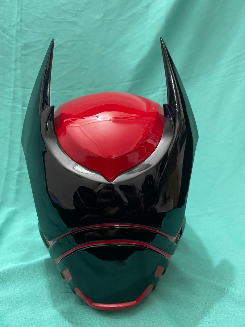 May include: A black and red helmet with a pointed design on the top. The helmet has a glossy finish and a red visor.