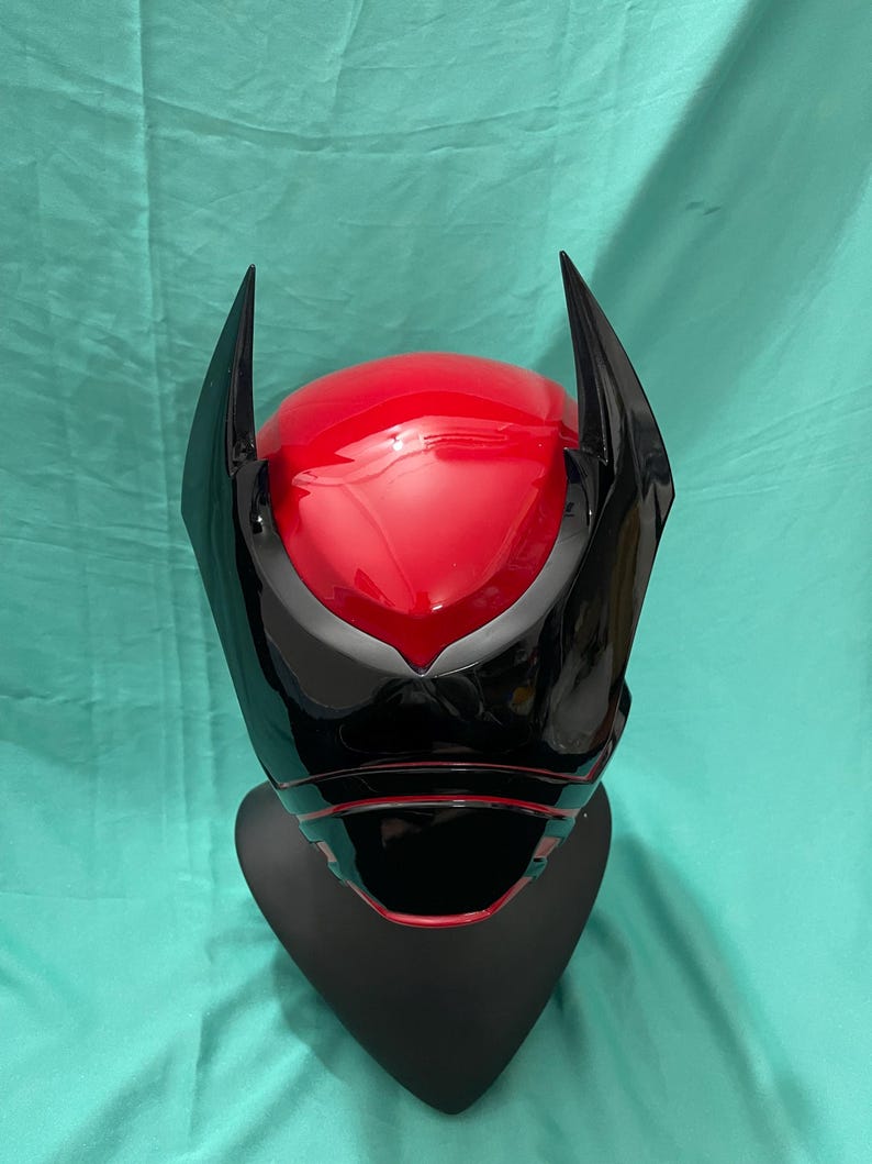 May include: A black and red plastic helmet with a pointed design on the top. The helmet has a black visor and a red interior.