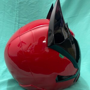May include: A red and black helmet with a pointed design on the top. The helmet has a glossy finish and a green accent on the front.