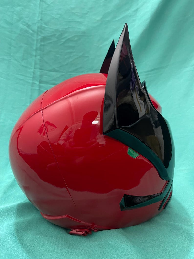 May include: A red and black helmet with a pointed design on the top. The helmet has a glossy finish and a green accent on the front.