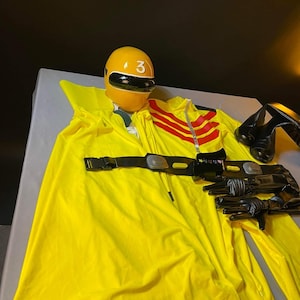 Puede incluir: Traje de superhéroe amarillo y negro con una capa, un cinturón negro y un casco amarillo con el número 3.