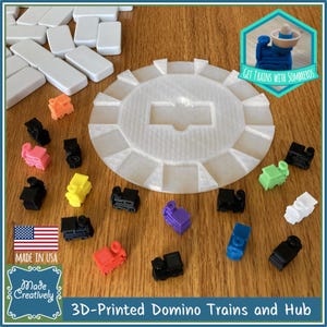 May include: A set of 3D printed domino trains and a hub. The trains are in various colors, including red, orange, yellow, green, blue, purple, and white. The hub is a white circular platform with slots for the trains to connect. The text "GET TRAINS WITH SOMBREROS" is visible in the image.