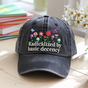 Op de afbeelding: Zwarte denim baseballpet met geborduurde bloemen en de tekst "Geradicaliseerd door elementaire fatsoen".