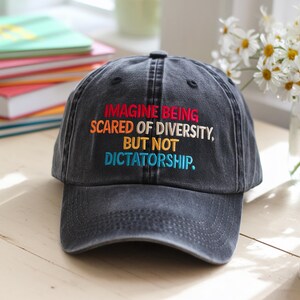 Op de afbeelding: Zwarte baseballpet met de tekst "Imagine being scared of diversity, but not dictatorship." geborduurd in regenboogkleuren.