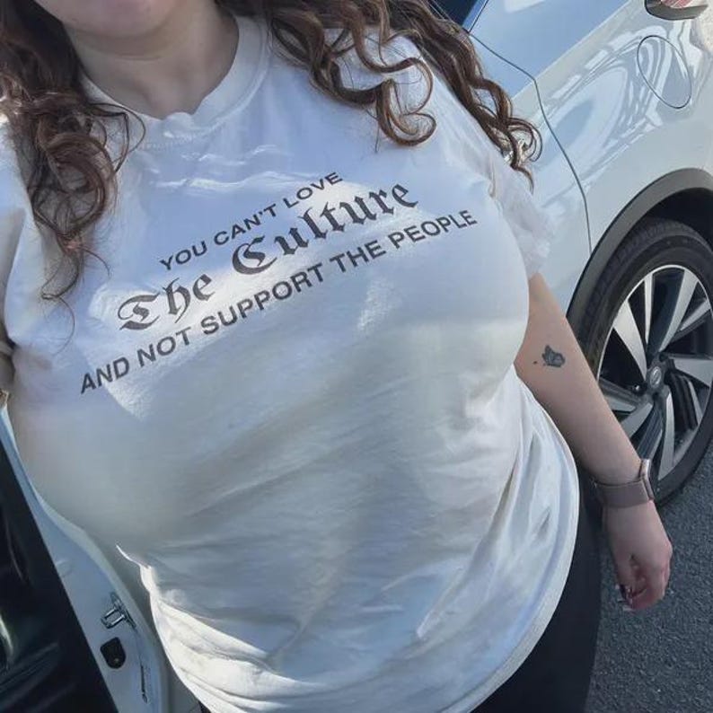 K&ouml;nnte beinhalten: Ein wei&szlig;es kurz&auml;rmeliges T-Shirt mit schwarzem Text auf der Brust, der lautet: "YOU CAN'T LOVE The Culture AND NOT SUPPORT THE PEOPLE." Das T-Shirt hat einen Rundhalsausschnitt und eine Standardpassform, wobei der Text in verschiedenen Schriftarten gedruckt ist.