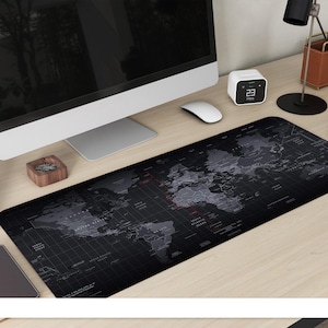 Può includere: Tappetino da scrivania nero con un design a mappa del mondo in tonalità di grigio. Il tappetino è rettangolare e copre una vasta area della scrivania. Sono visibili un monitor del computer, un mouse e altri accessori da scrivania.