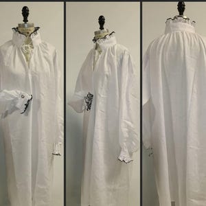 May include: A white long-sleeved shirt featuring a high ruffled collar with a drawstring tie, long billowy sleeves with ruffled cuffs, and black trim detailing on the collar and cuffs, displayed on a mannequin from front, side, and back views.