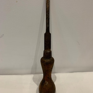 May include: A vintage flathead screwdriver featuring a weathered, dark brown wooden handle with a bulbous, ergonomic shape and a long, oxidized metal shaft showing signs of rust and wear along the flat tip and the main body of the steel blade.