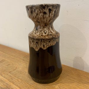 May include: A brown ceramic vase with a distinctive form. The vase features a dark brown base and a lighter brown, textured top. The vase is placed on a wooden surface.