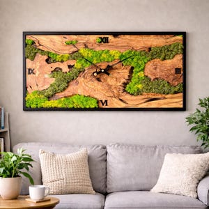 Puede incluir: Un reloj de pared rectangular con marco negro. La esfera del reloj presenta un diseño de veta de madera natural con detalles de musgo verde. Los números romanos son visibles en las posiciones de las 3, 9 y 12 en punto. Las manecillas del reloj son negras.