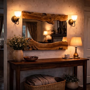 May include: A rustic entryway scene featuring a large, live-edge wooden mirror above a dark wood console table. The table holds a lamp, bowl, and vase. Two sconces flank the mirror, and a woven basket sits below. The room is warmly lit.