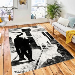 Puede incluir: Alfombra en blanco y negro con una ilustración estilizada de dos gatos, uno negro y uno blanco, caminando por un sendero. La alfombra tiene un fondo blanco y el texto "Manet" está impreso en la esquina inferior izquierda.